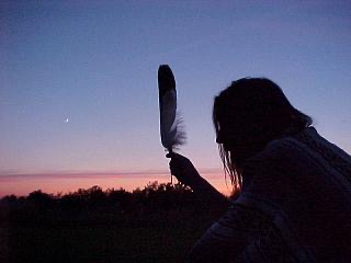 Sillouette of person holding a feather against a sunset 