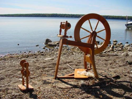 A spinning wheel on the edge of a lake with wool being spun on a spindle