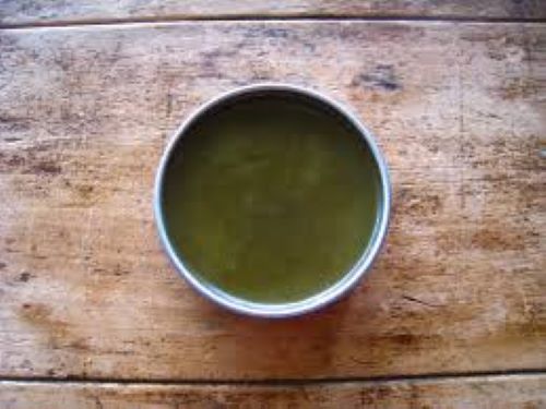 A jar of Black Walnut & Tea Tree Salve resting on a wooden countertop.  