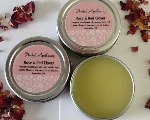 Three Rose & Red Clover salves surrounded by red rose petals.